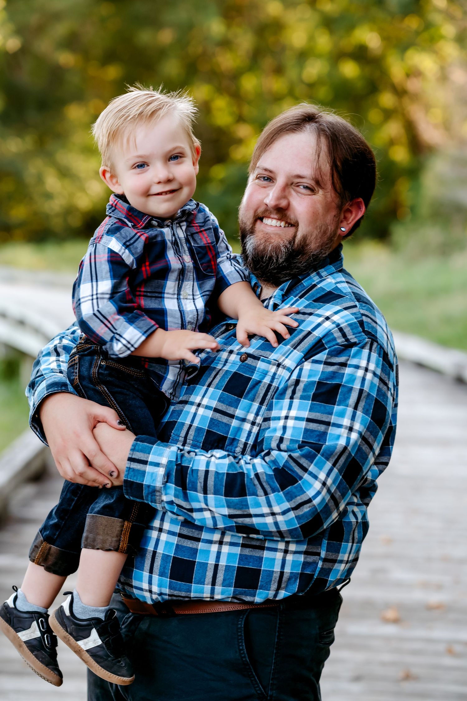 A playful moment captured between parent and child wearing matching plaid shirts in an outdoor autumn setting.