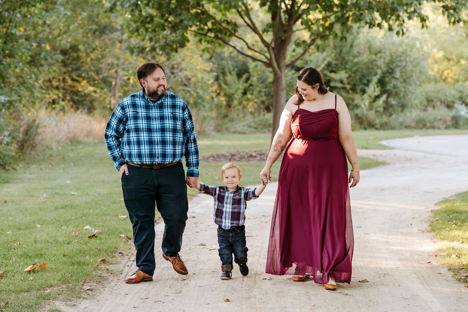 A family walks together on a tree-lined path during a fall photo session in matching burgundy and blue outfits.