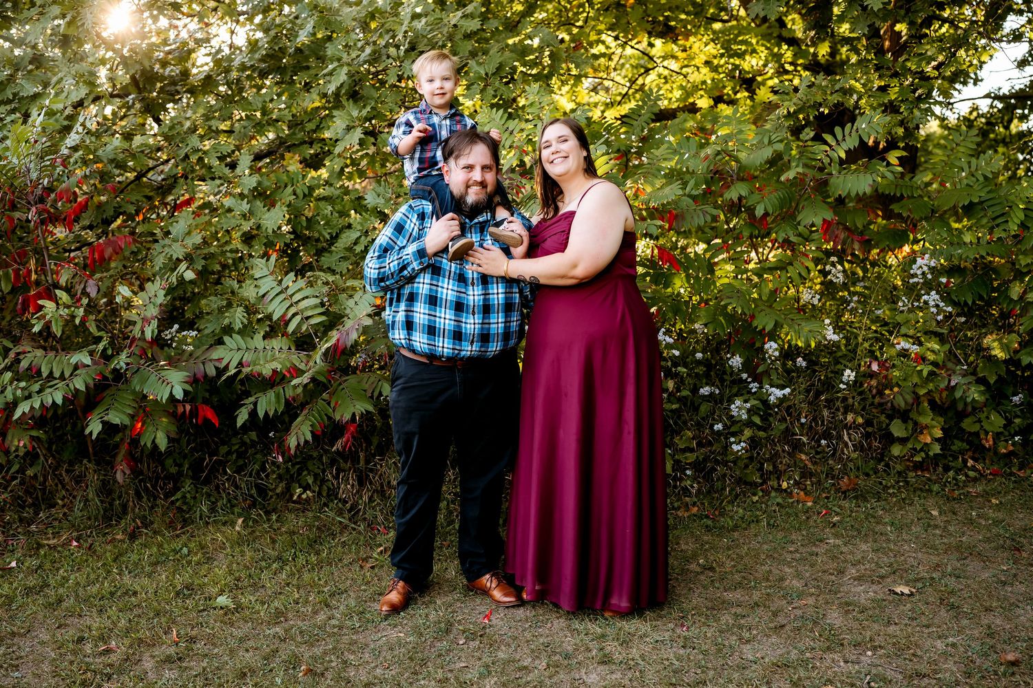 A group gathers for outdoor autumn portraits among trees and foliage with sunlight filtering through the branches.