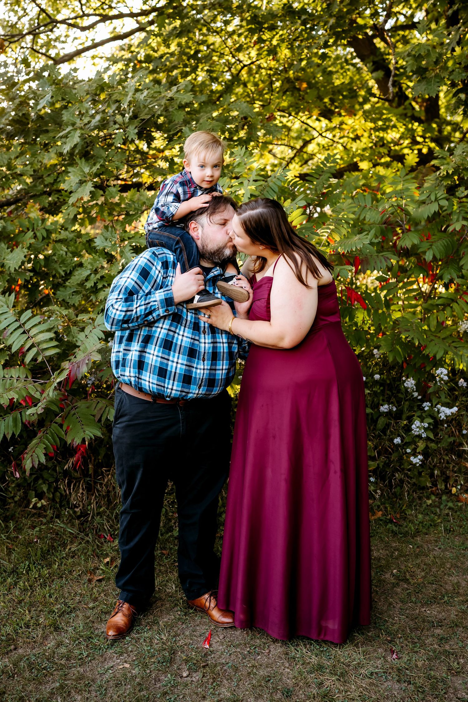 A couple in a burgundy dress and plaid shirt share romantic moments in a garden setting with autumn foliage.