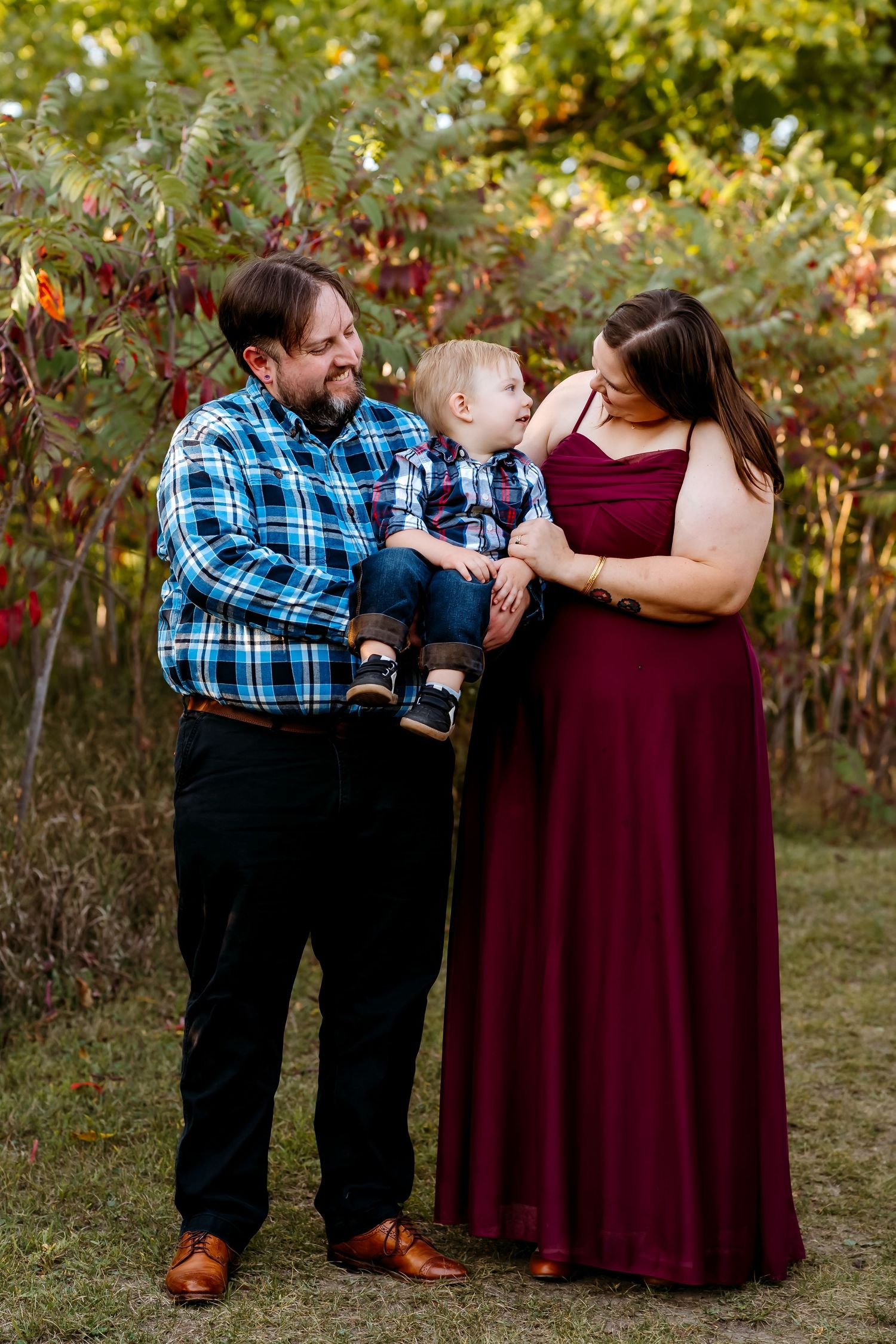 A couple in burgundy and plaid share a tender moment during their autumn outdoor photo session.