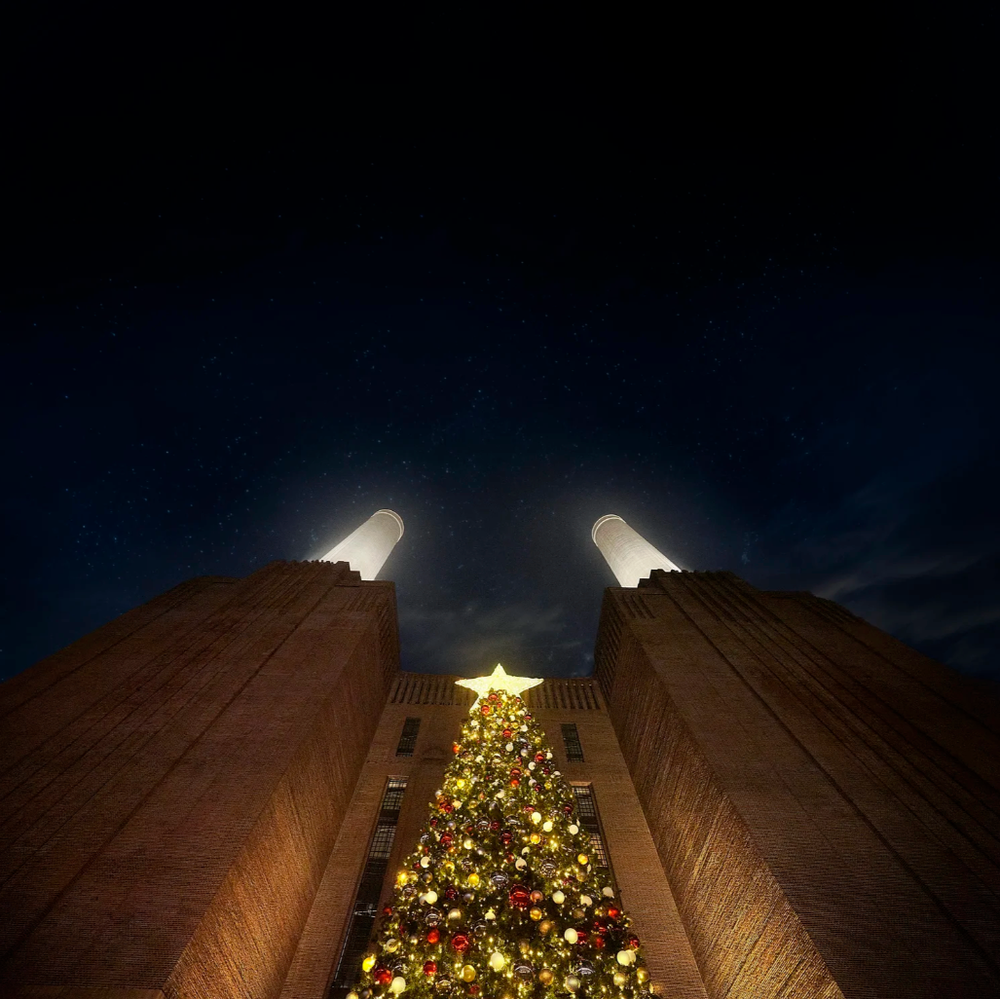 Illuminated Christmas tree with star topper viewed between tall buildings at night.