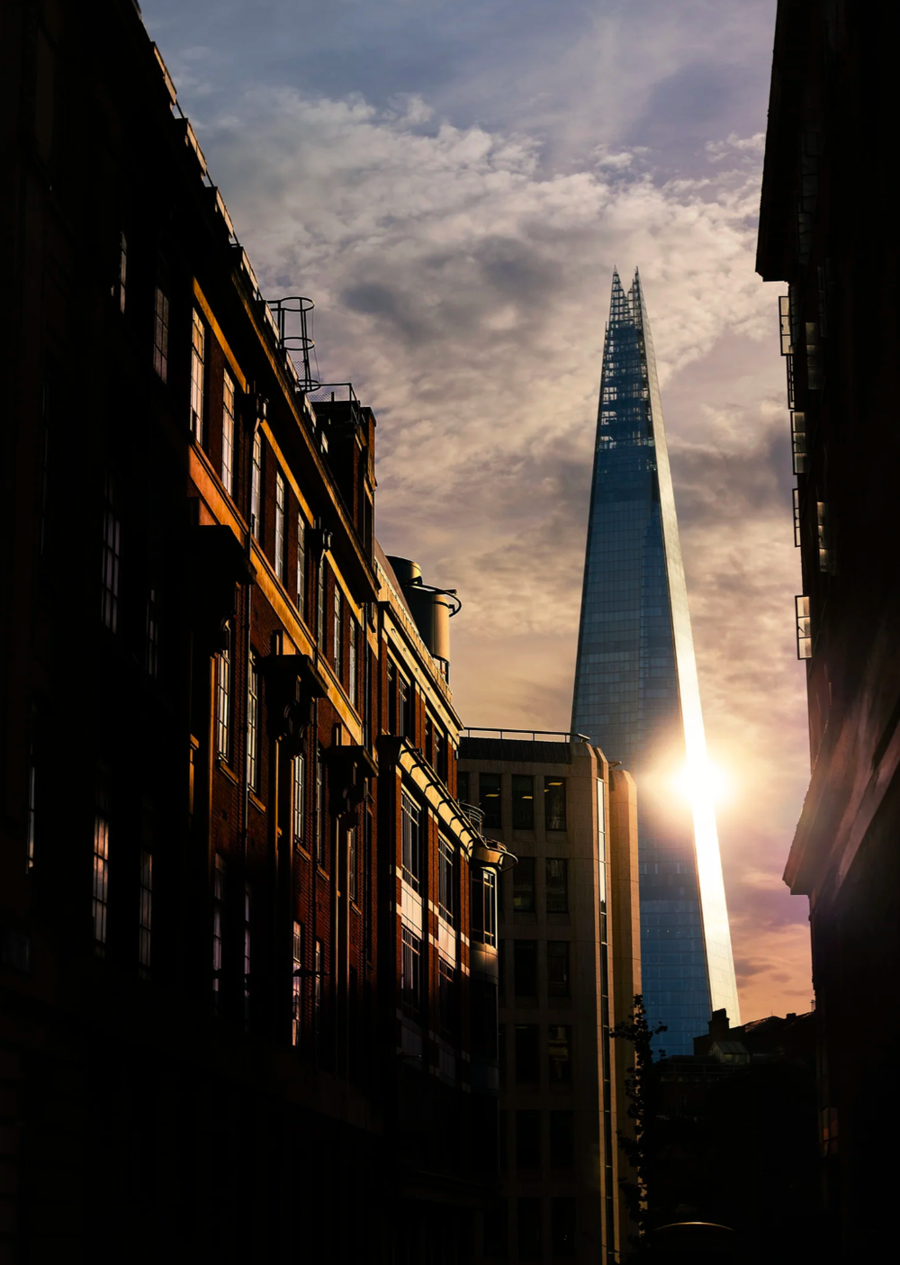 Modern glass skyscraper silhouetted against dramatic sunset sky in urban setting.