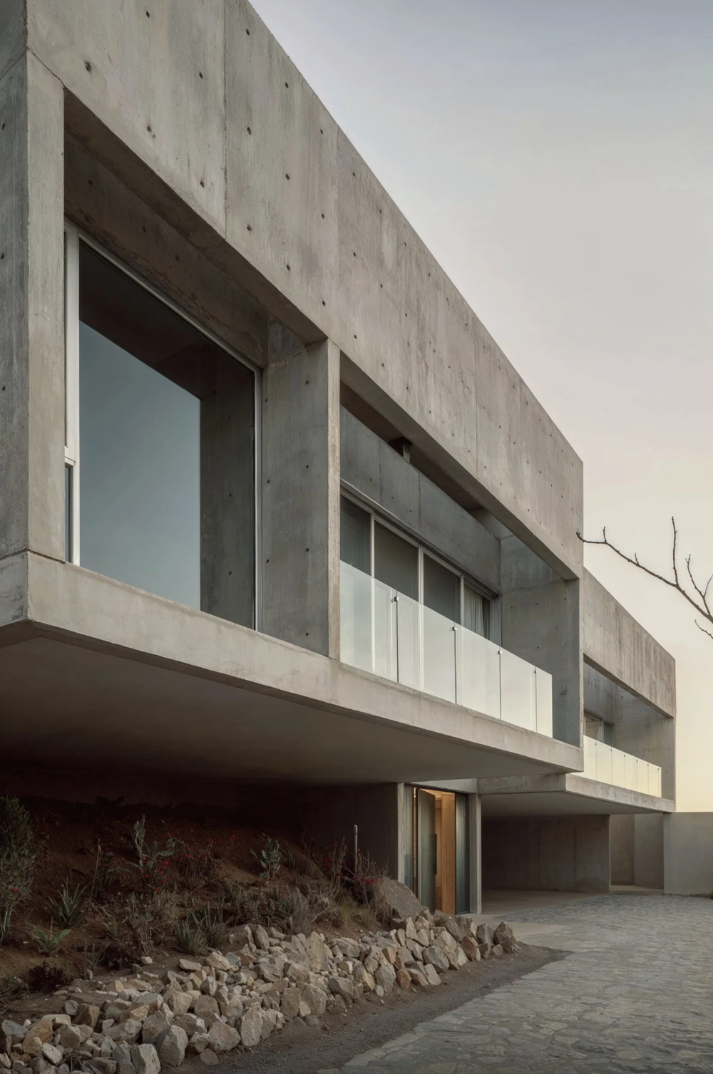 Modern concrete building with glass windows and stone foundation in minimalist design.
