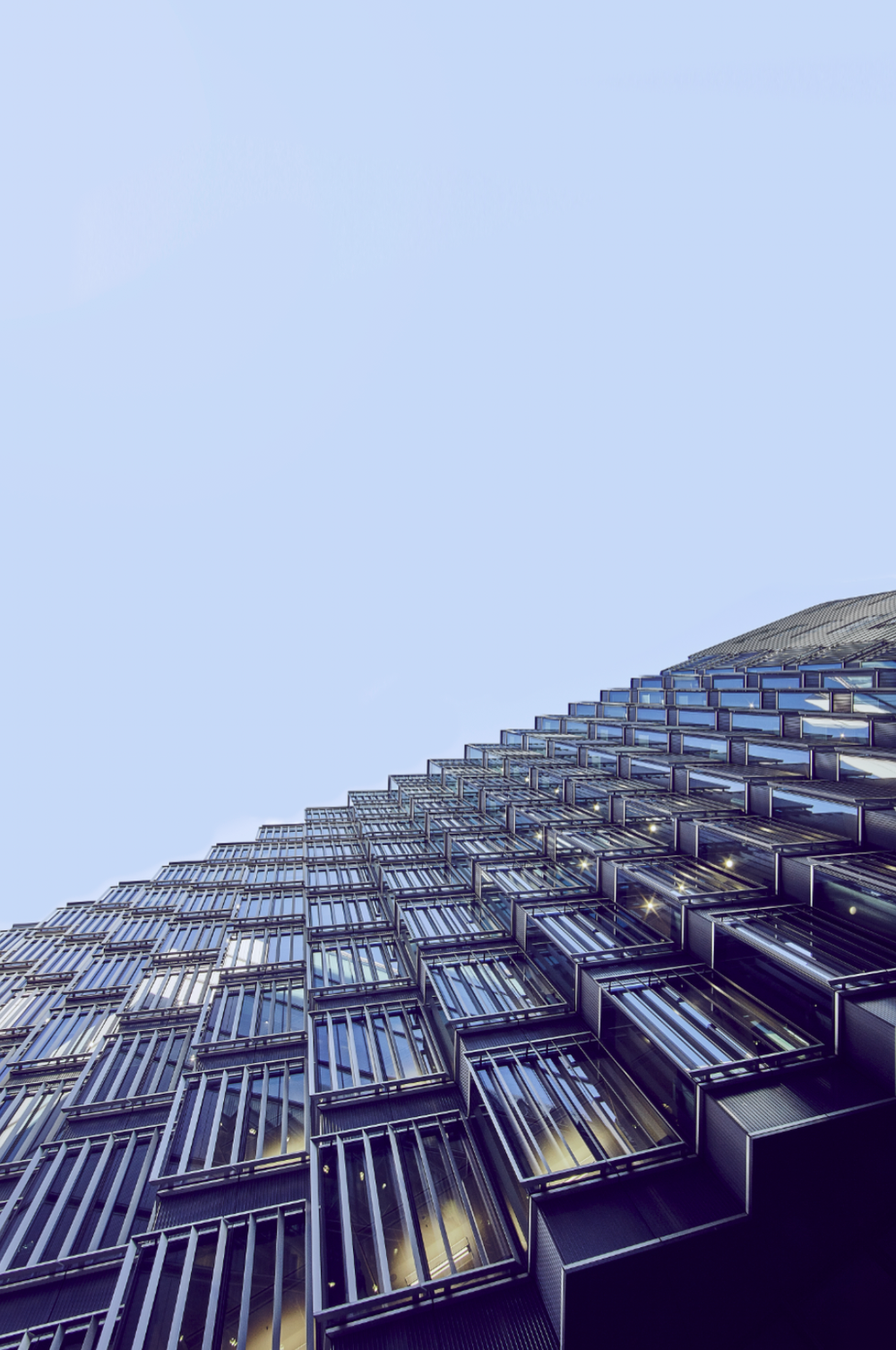 Modern building facade with geometric patterns photographed from below against light blue sky.
