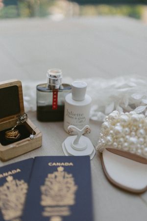 Wedding accessories including Canadian passports, pearls, and perfume arranged on white surface.