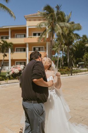 Romantic moment captured at a tropical resort with palm trees and beige buildings in background.