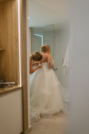 Wedding dress preparation in modern white bathroom with mirror and wooden accents.