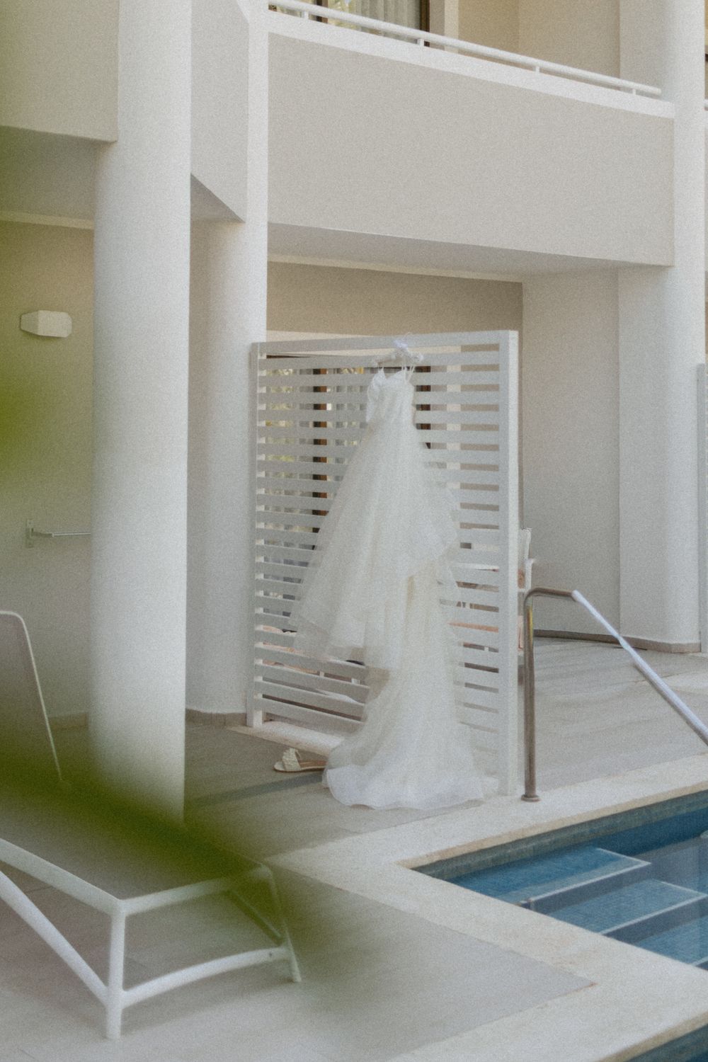 White wedding dress hanging in modern spa area with pool and white columns.