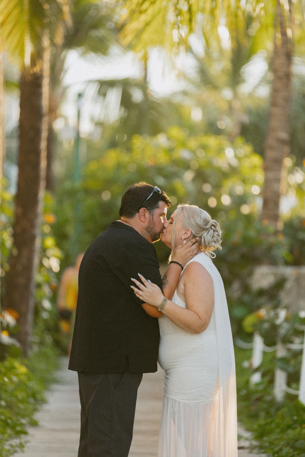 Intimate moment shared between couple on a palm-lined path at sunset.