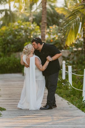 A romantic moment captured on a wooden boardwalk surrounded by tropical palm trees and lush greenery.