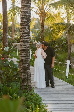 Couple sharing an intimate moment on a palm-lined wooden walkway at sunset.