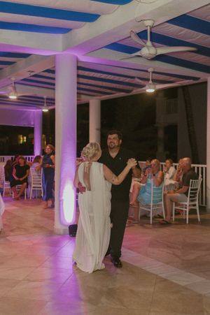 Couples dancing in an elegant venue with purple mood lighting and white columns.