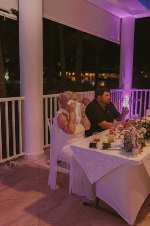 Reception tables set with white linens on a covered patio with purple ambient lighting.