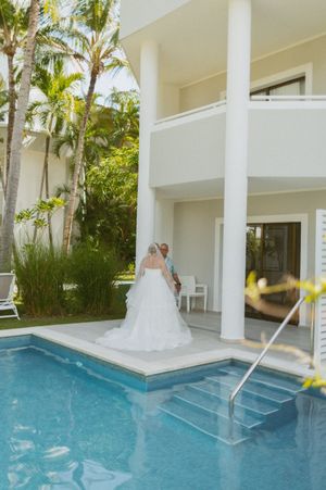 Elegant white wedding dress against modern architecture with swimming pool and palm trees.