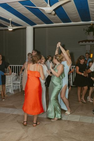 Wedding guests dancing in colorful dresses under blue and white striped ceiling.