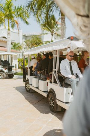 Golf carts lined up at a tropical resort venue with palm trees and white buildings in the background.