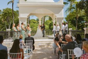 White Mediterranean-style wedding gazebo with arches and columns surrounded by tropical landscaping.