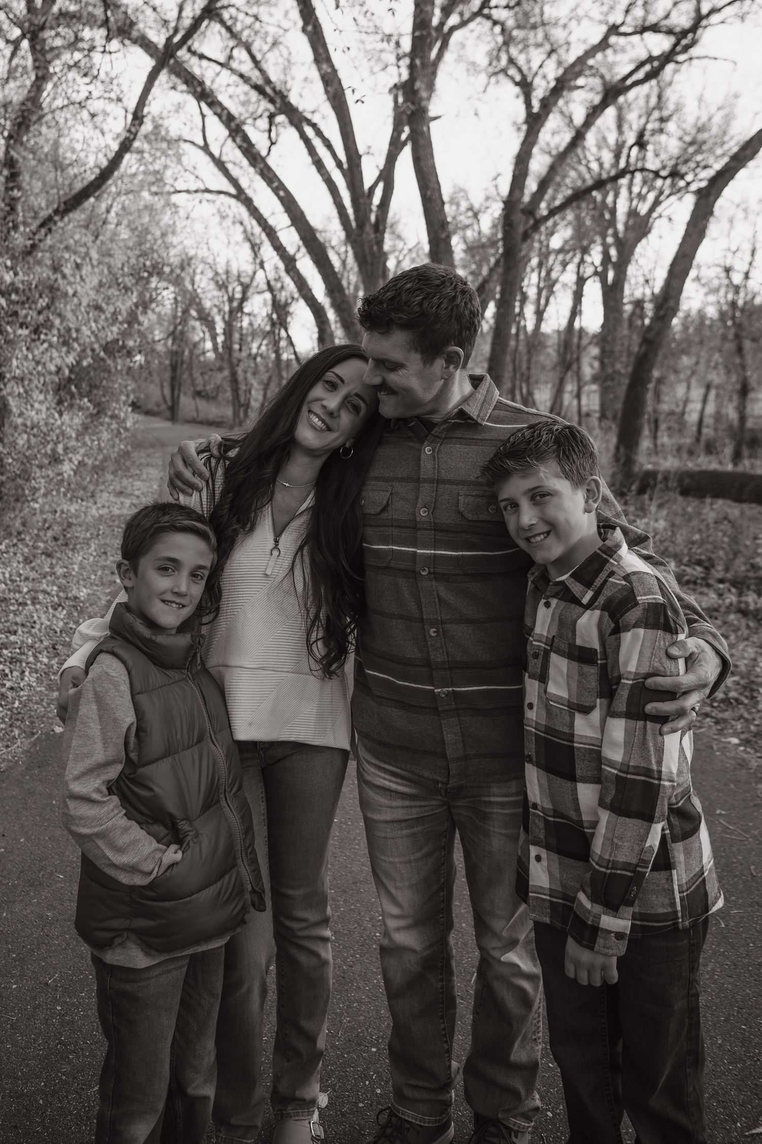 A family of four shares a candid moment together on a path surrounded by bare trees.