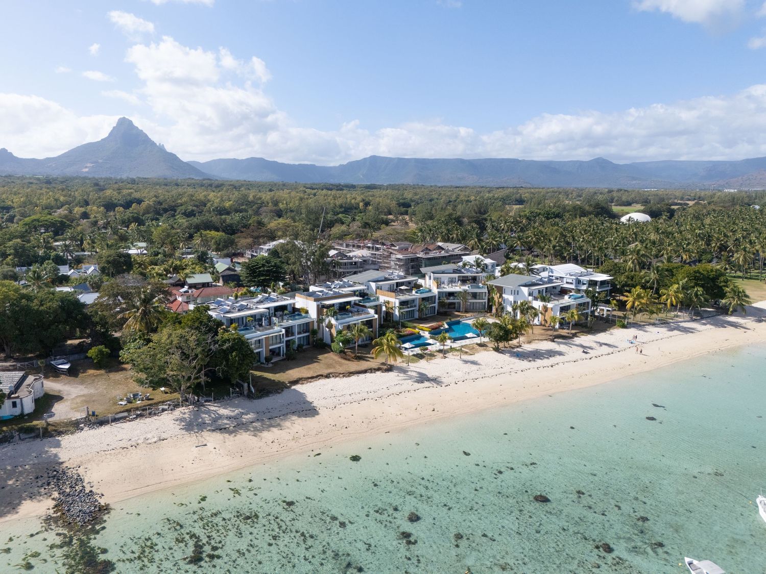 Aerial panoramic view of a tropical beach resort with turquoise waters, white sand, and coastal buildings in Mauritius.