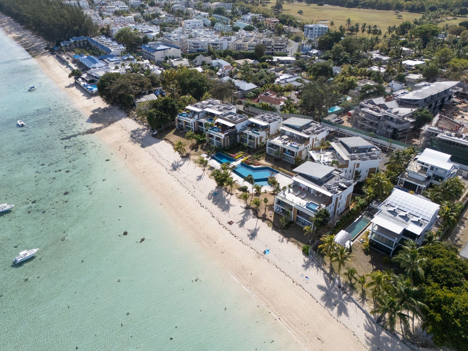 Aerial drone view of a tropical beach resort with white sand, turquoise water, and beachfront properties.