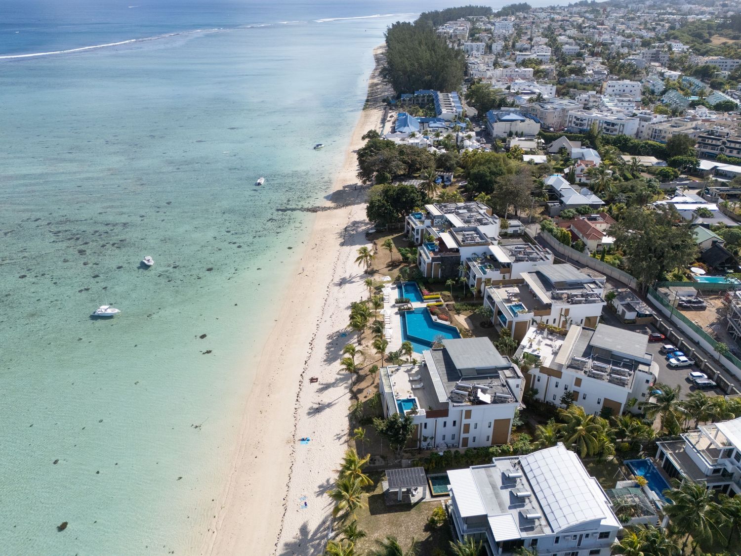 Aerial view of a pristine white sand beach with turquoise waters and beachfront resorts in a tropical coastal town.