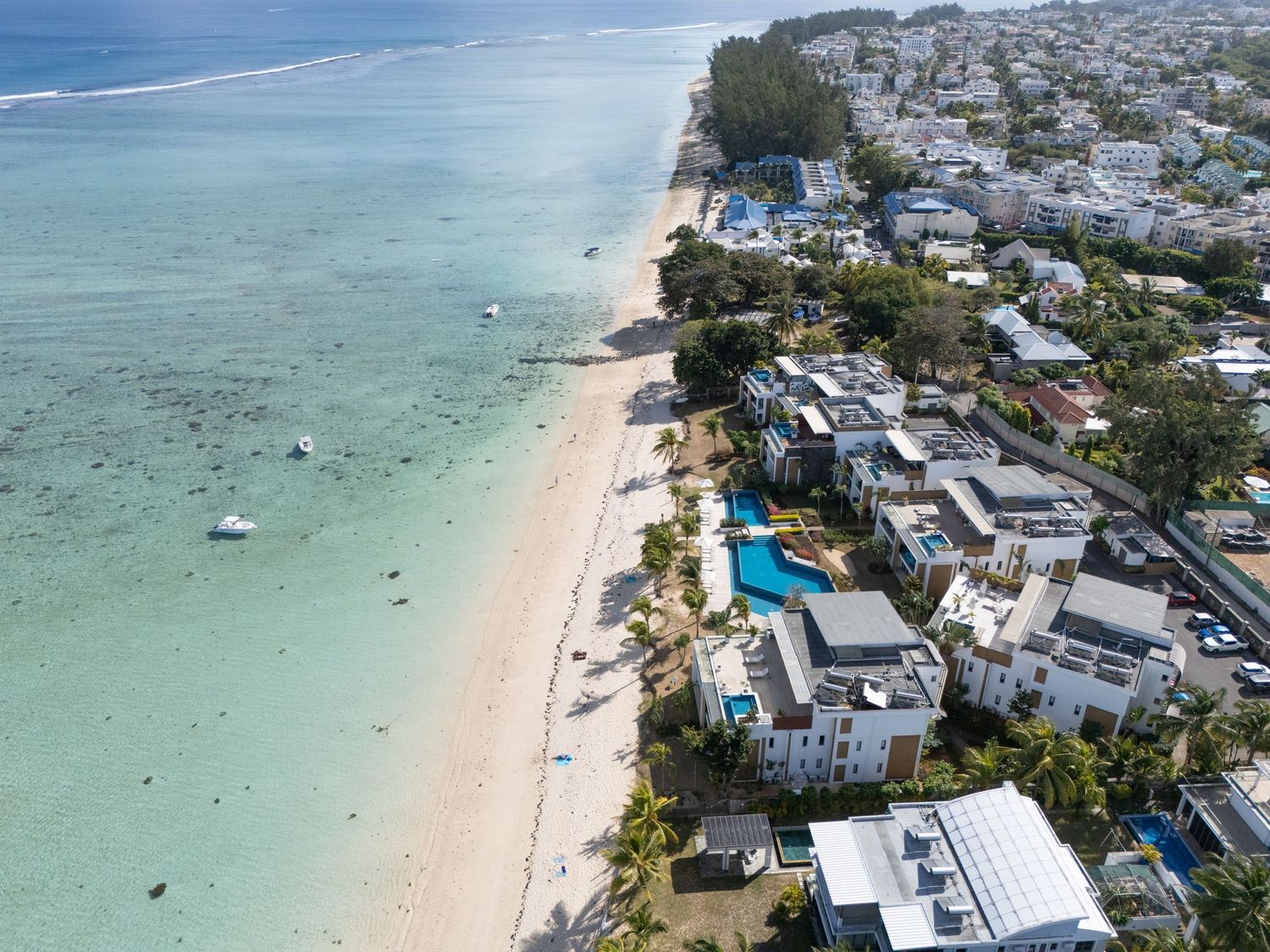 Aerial view of turquoise waters and beachfront properties along a pristine white sand beach in a tropical coastal town.
