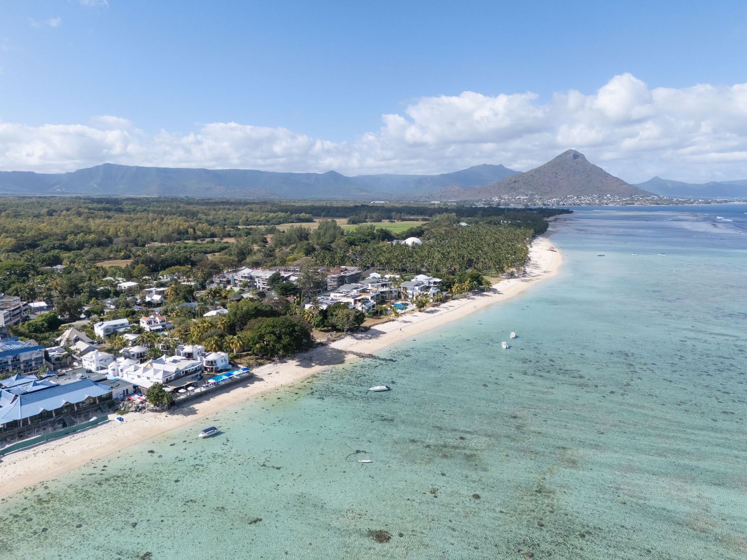 Aerial panoramic view of a tropical coastline with turquoise waters, sandy beaches, and lush green landscape in Hawaii.