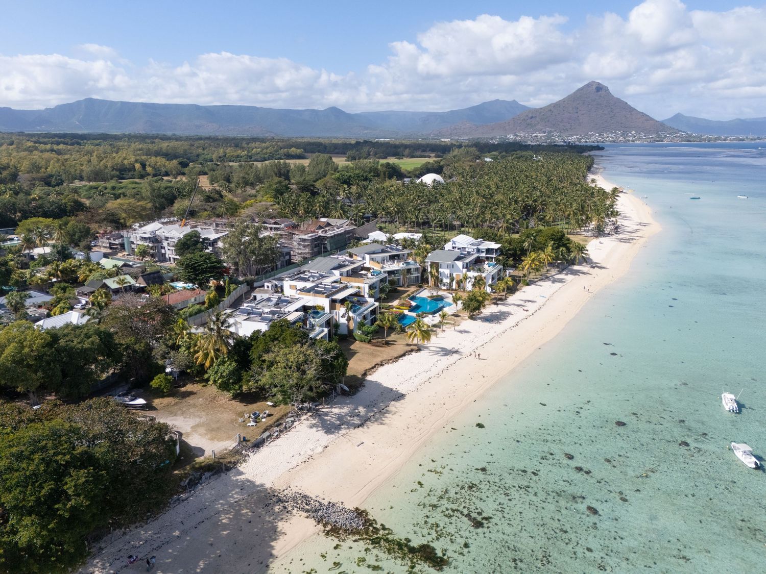 Aerial panoramic view of a pristine beach resort with white sand, turquoise waters and coastal buildings in Mauritius.