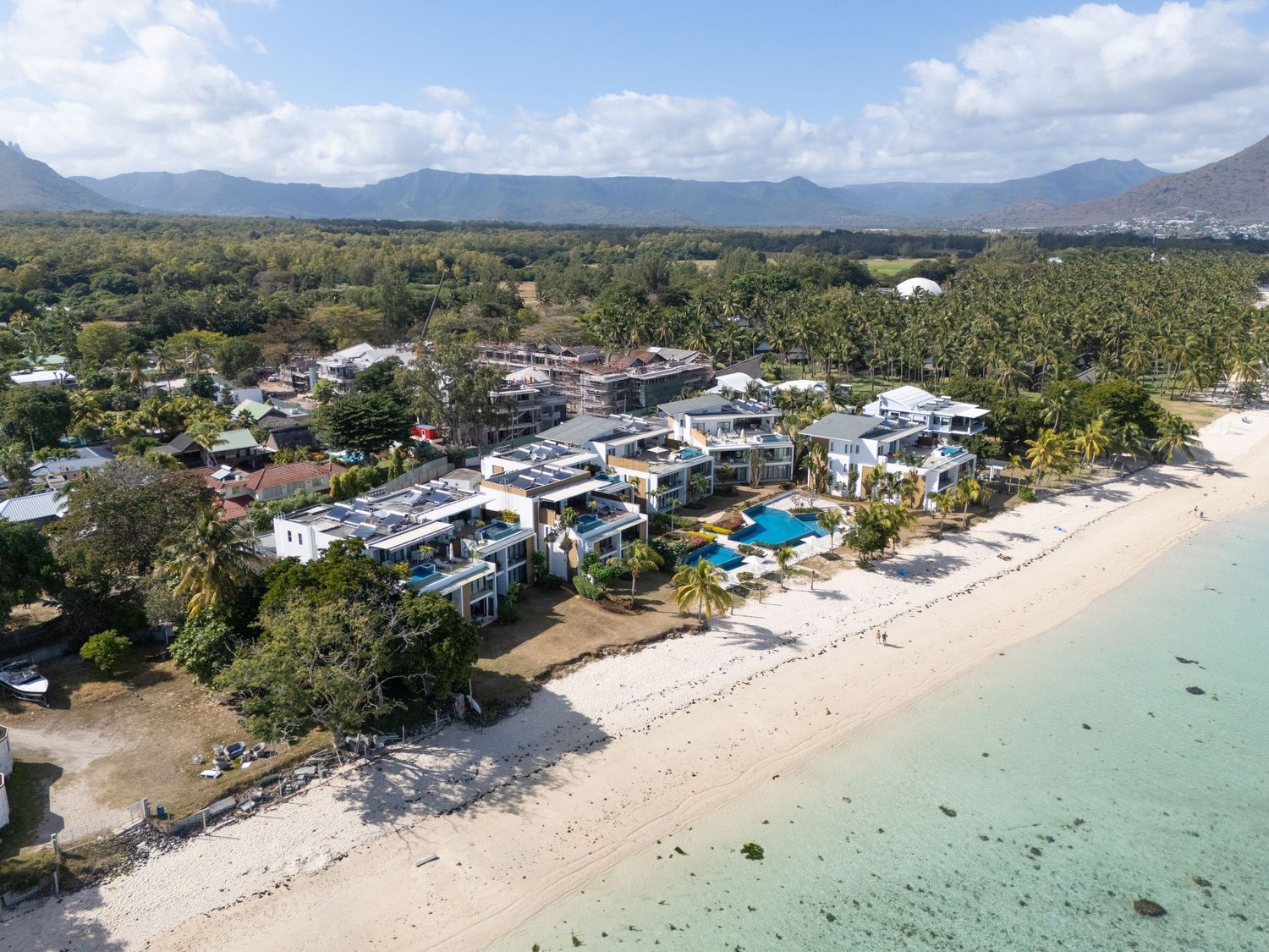 Aerial panoramic view of a tropical beachfront resort with turquoise waters, white sand beaches and coastal buildings.