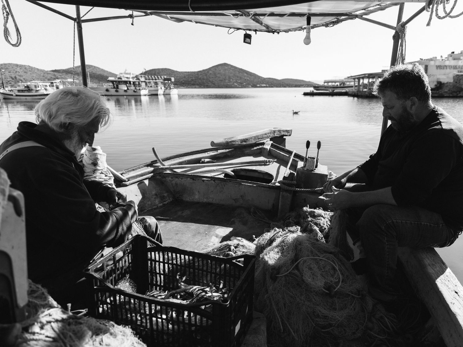 Fishermen sitting on a traditional fishing boat in Elounda harbour, Crete, calm morning light and quiet coastal life