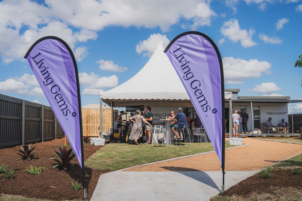 Purple promotional flags wave in front of new residential construction sites under a bright blue sky with white clouds.