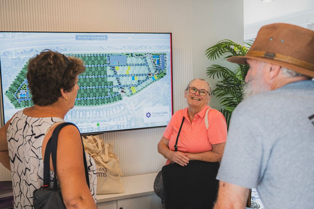 Three people having a discussion while looking at a property map displayed on a wall-mounted screen in an office setting.