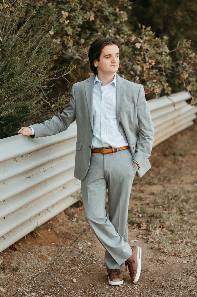 Casual formal fusion outfit featuring a grey suit, light blue shirt, and brown leather accessories photographed outdoors.