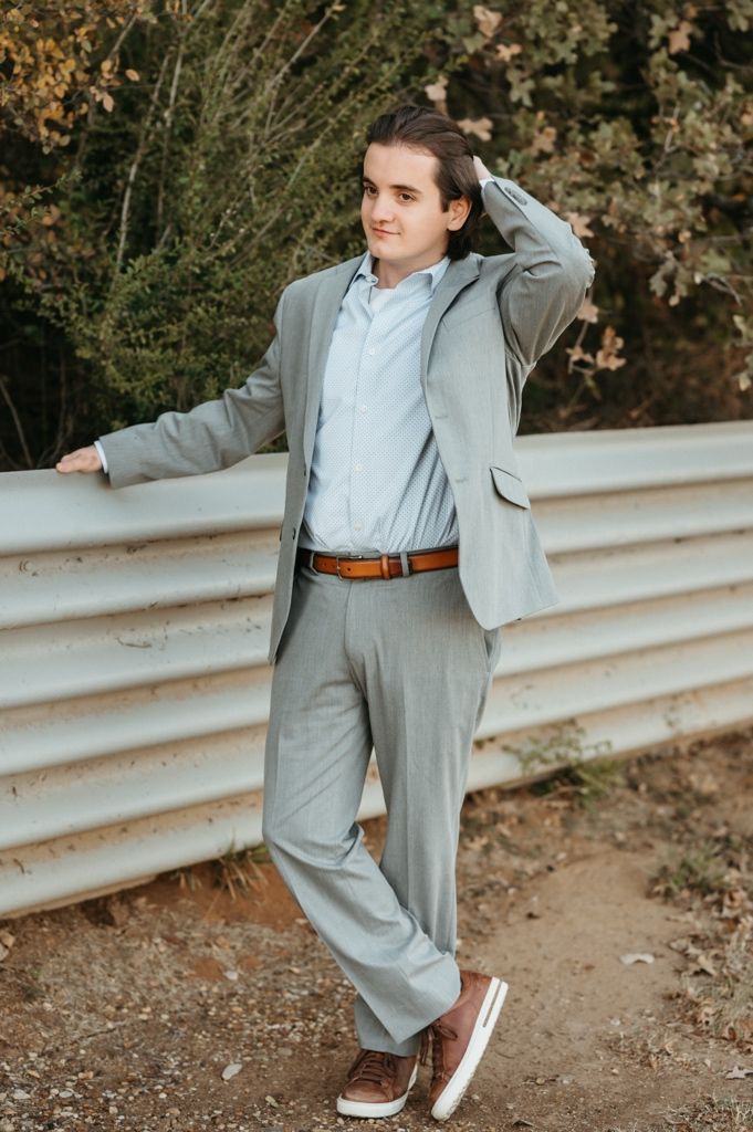A stylish grey suit ensemble paired with casual sneakers is modeled against a natural outdoor backdrop with guardrails.