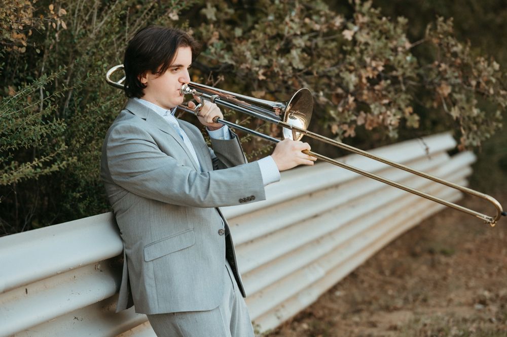 A person in a gray suit jacket stands on wooden steps while holding a camera in a natural outdoor setting.