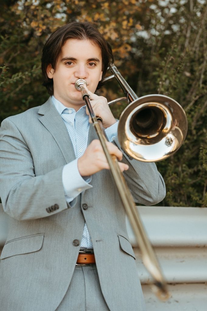 Close-up shots of a trombonist performing while wearing a light gray suit outdoors.