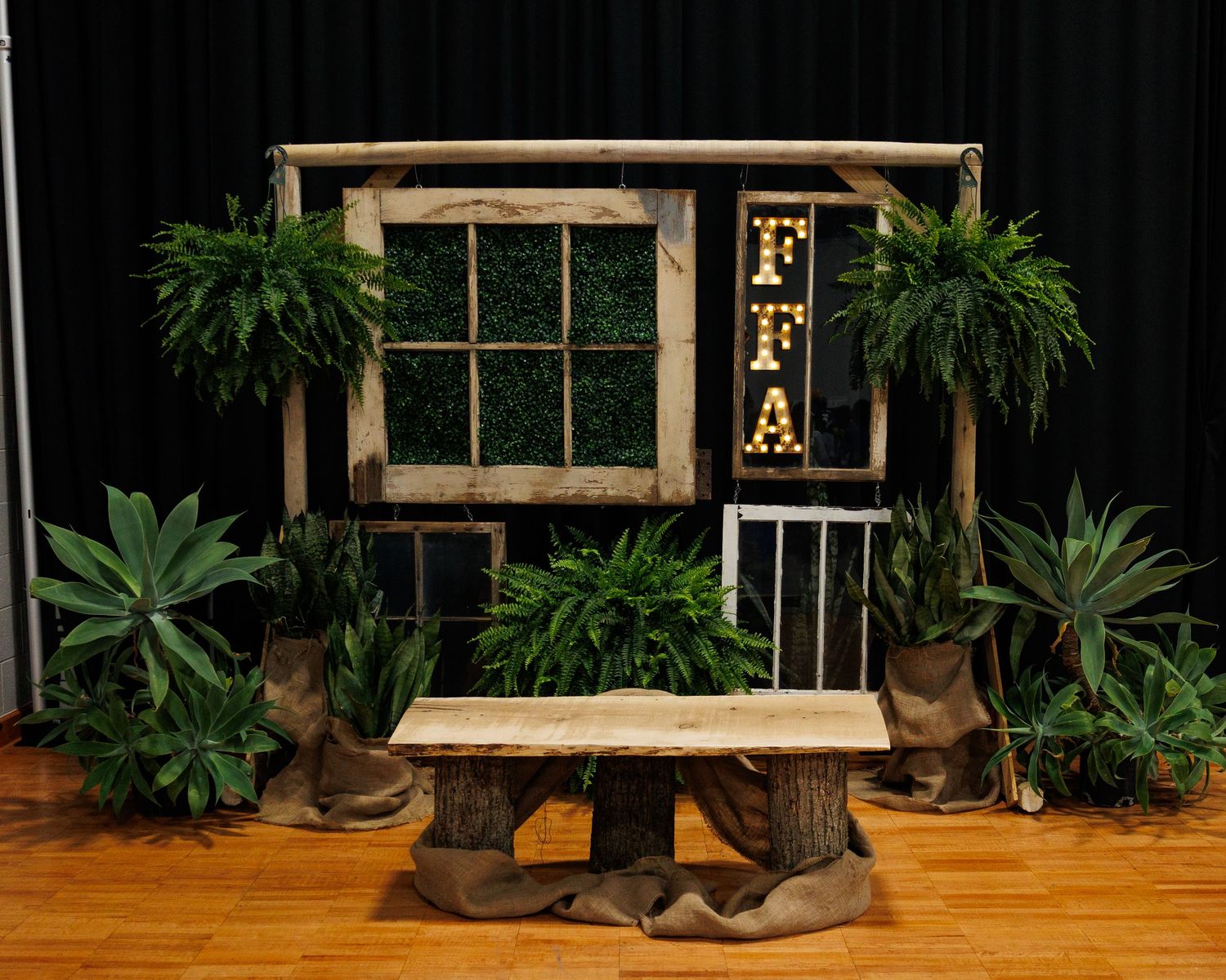 Rustic wooden bench with cowboy boots displayed against a dark backdrop surrounded by lush green plants.