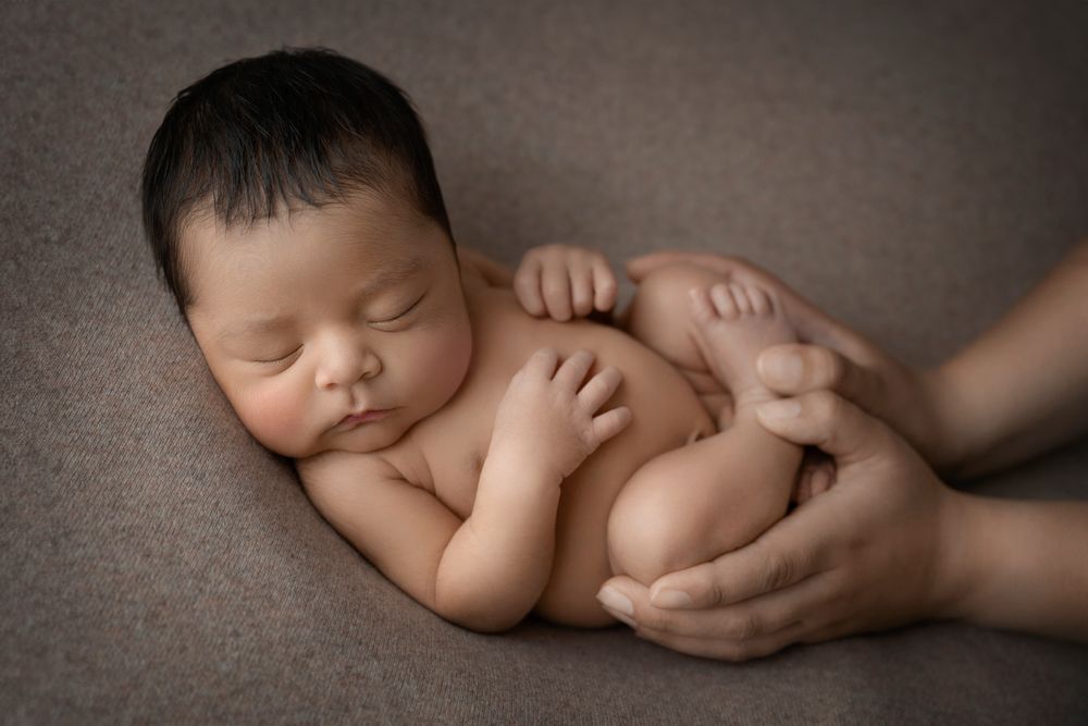 Newborn baby sleeping peacefully while being gently held by adult hands.