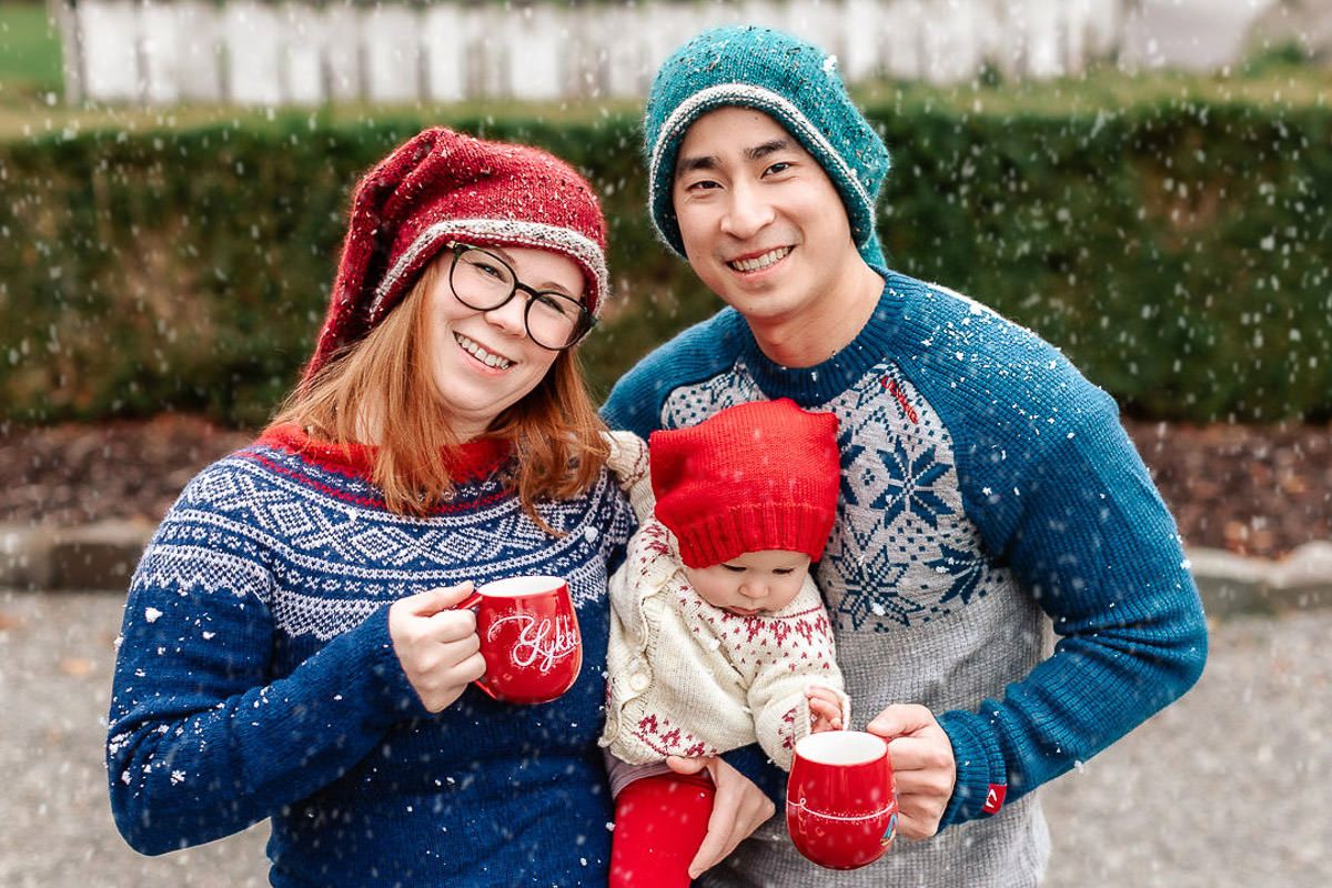 Familie på julekortfotografering på Ålgård hos Ørstavik Foto. Snøen daler og mor og far ser i kamera mens baby ser på julekoppene de holder.