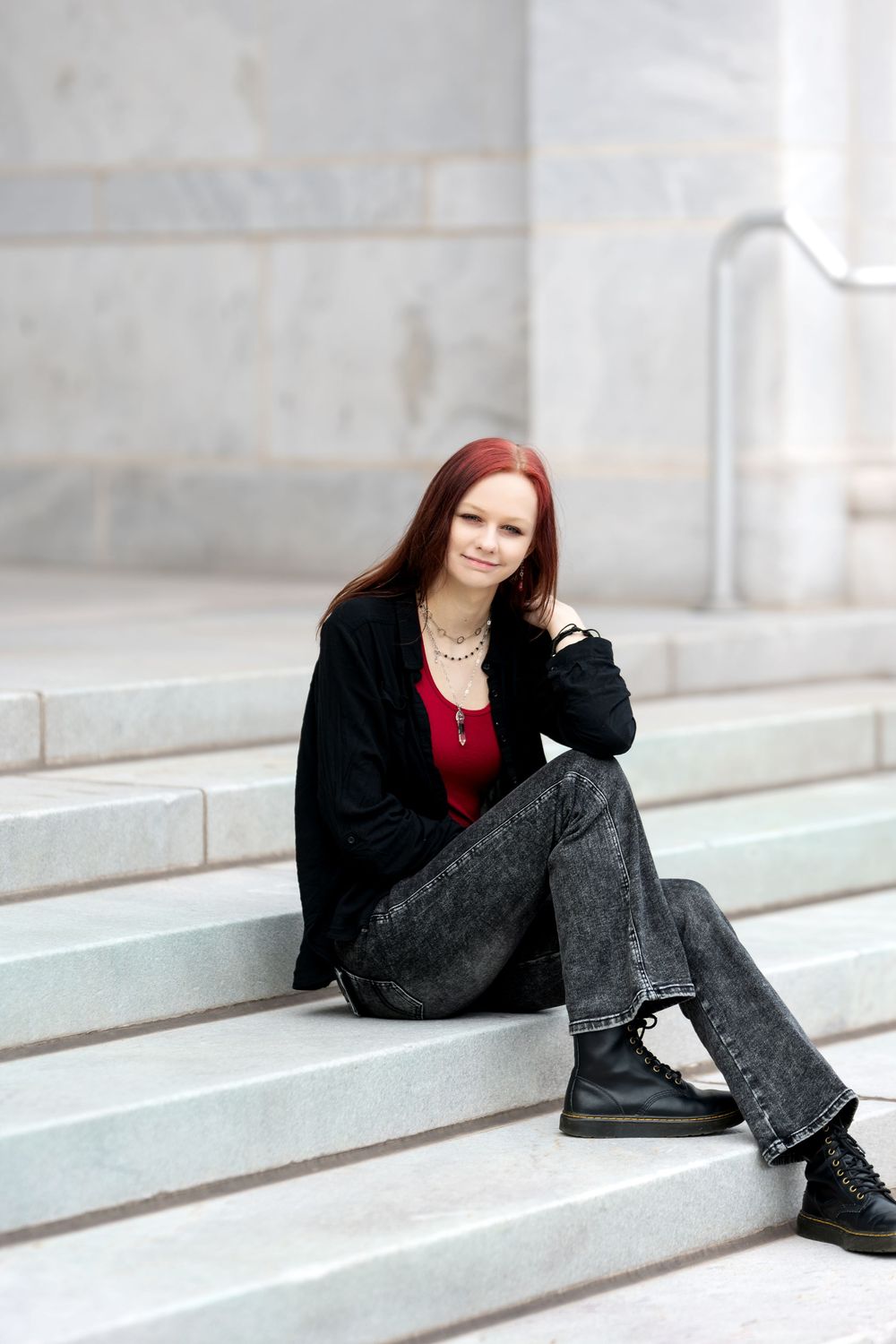 Redhead teen girl sitting on marble steps in black jacket and jeans.