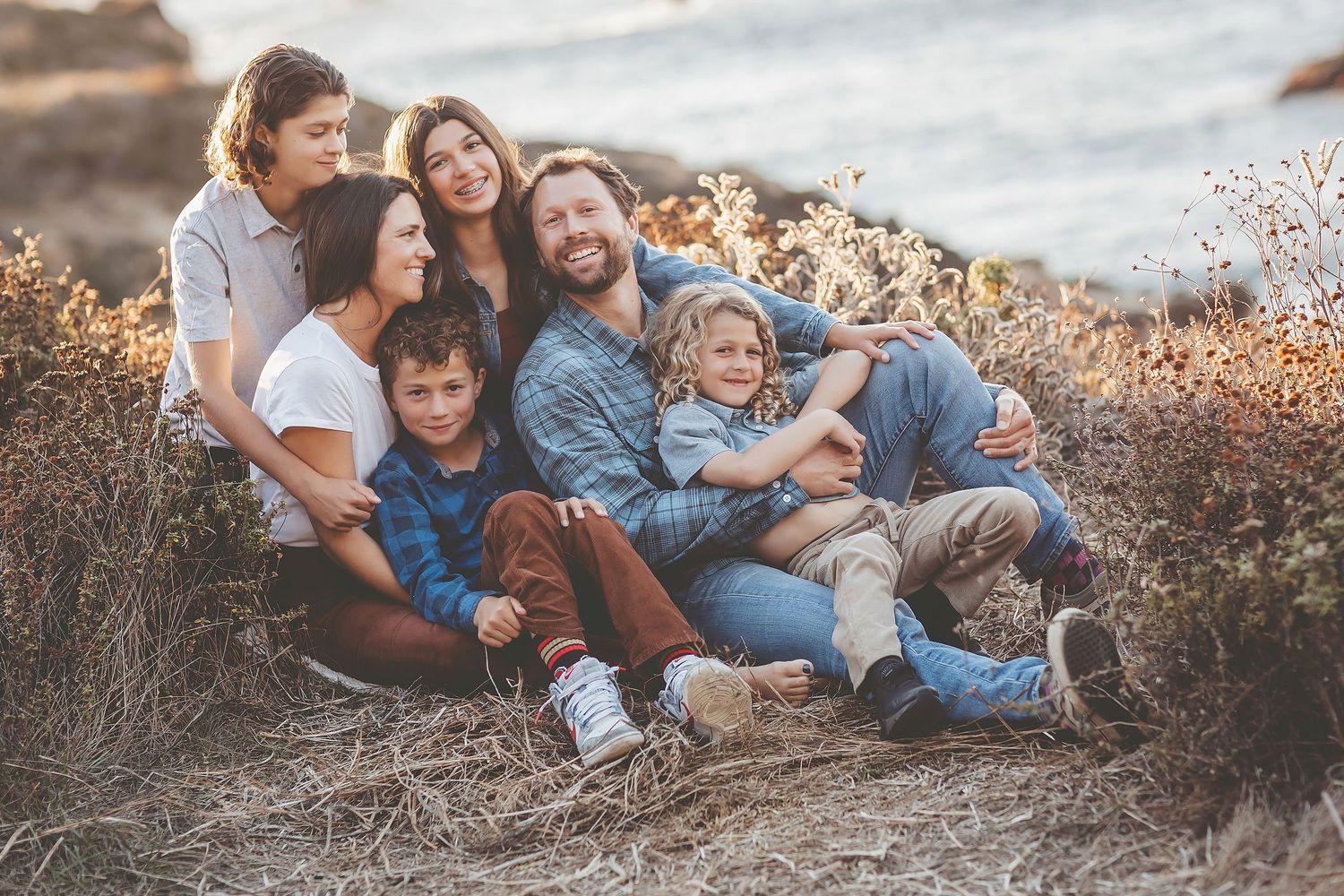 A family sits together outdoors during golden hour while sharing loving moments in a natural setting.