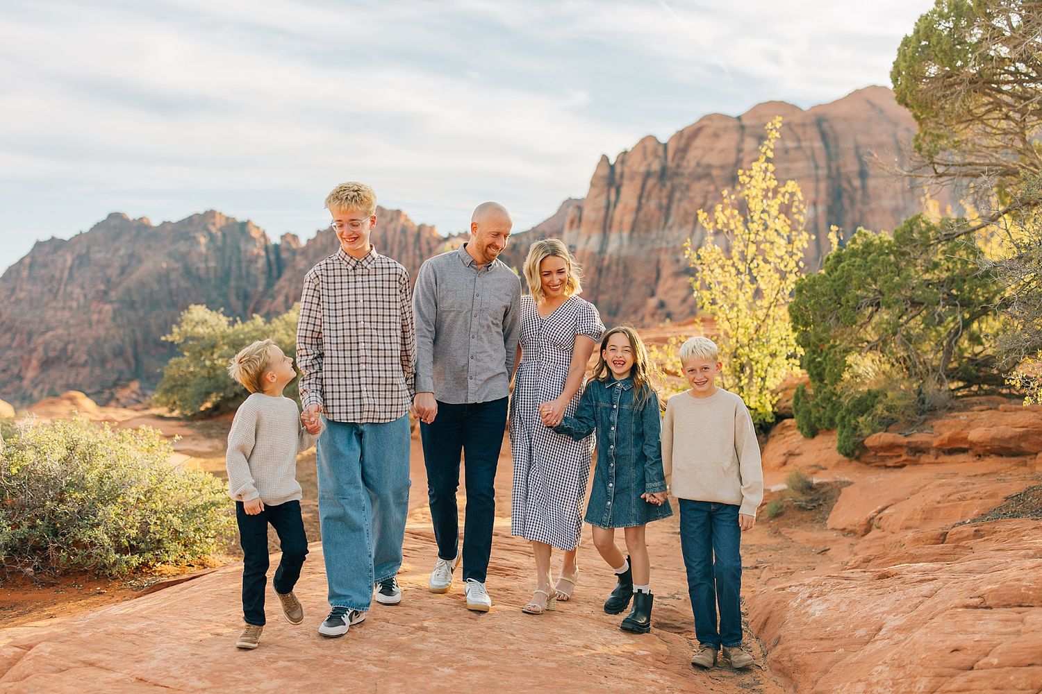 Family walking together on red rock trail with towering canyon walls in the background.
