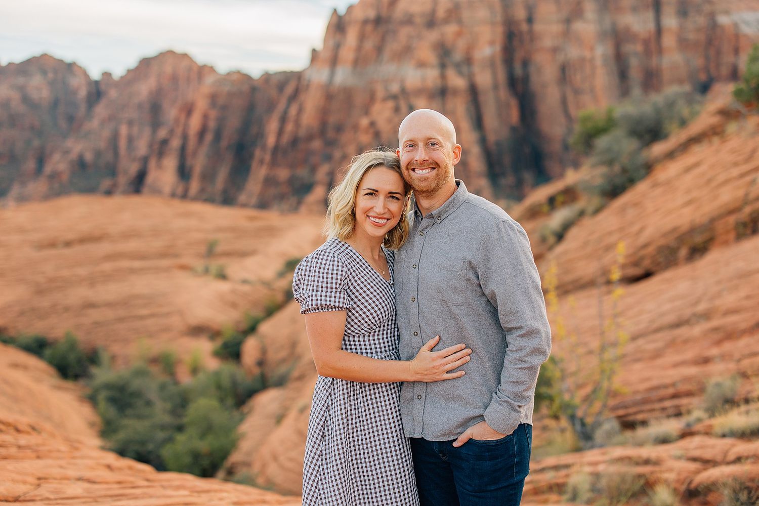 Couple in coordinating outfits embracing against dramatic red rock canyon landscape.