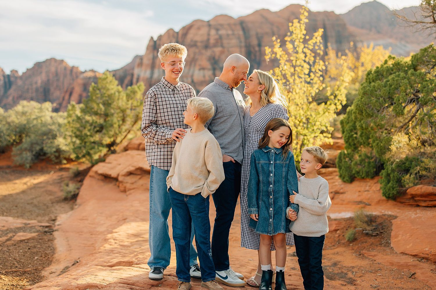 Family group standing together on red rock trail with sunlit desert landscape behind them.