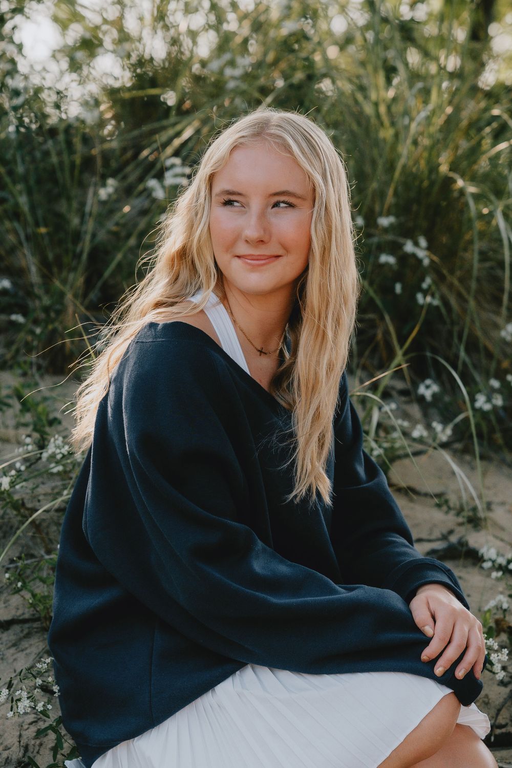 A casual outdoor portrait featuring a navy sweater and white skirt against a natural background with greenery.