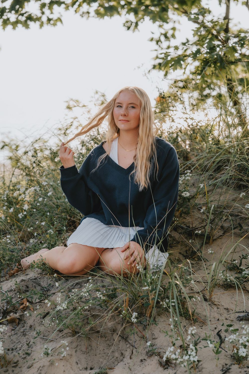 Portrait session on a grassy hillside at sunset wearing a navy sweater and white skirt.