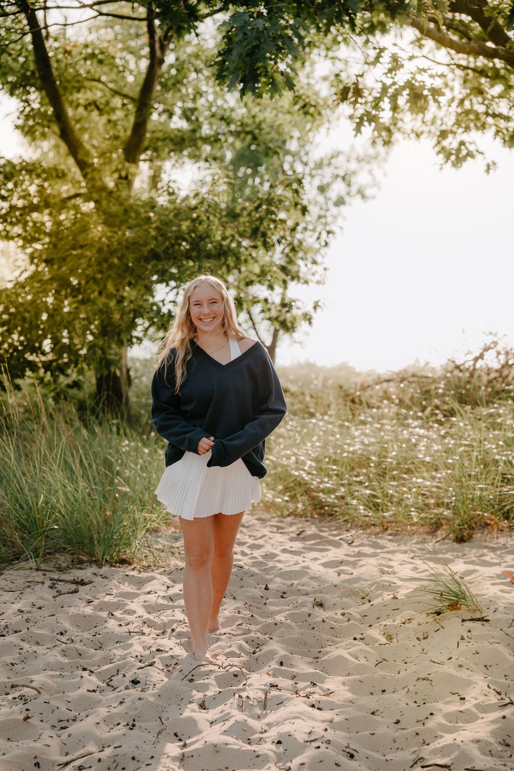 A casual beach portrait featuring a navy sweater and white skirt against a natural sandy backdrop with trees.