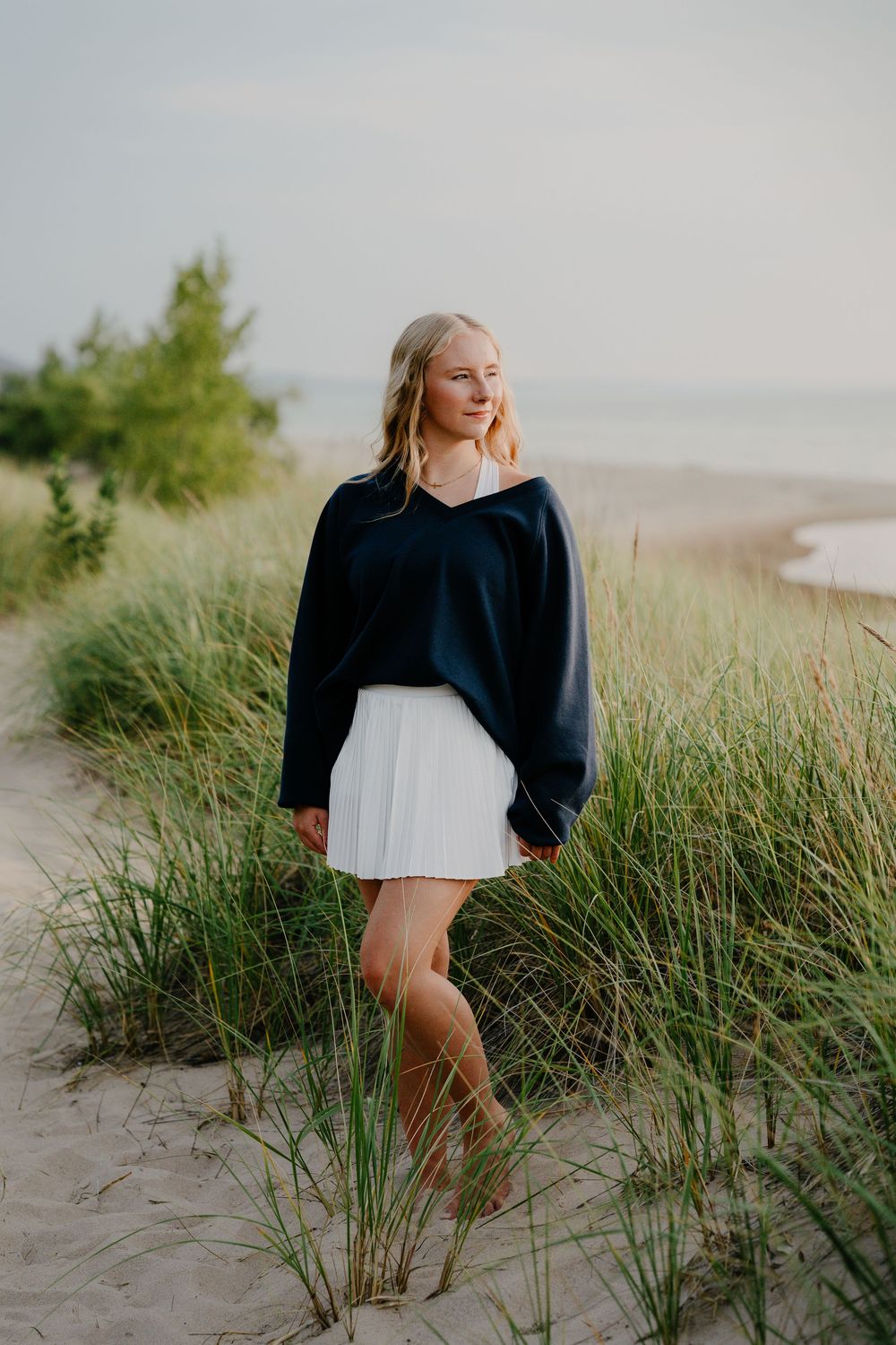 A beachside fashion photo showing a navy sweater and white skirt ensemble among coastal dunes and grass.