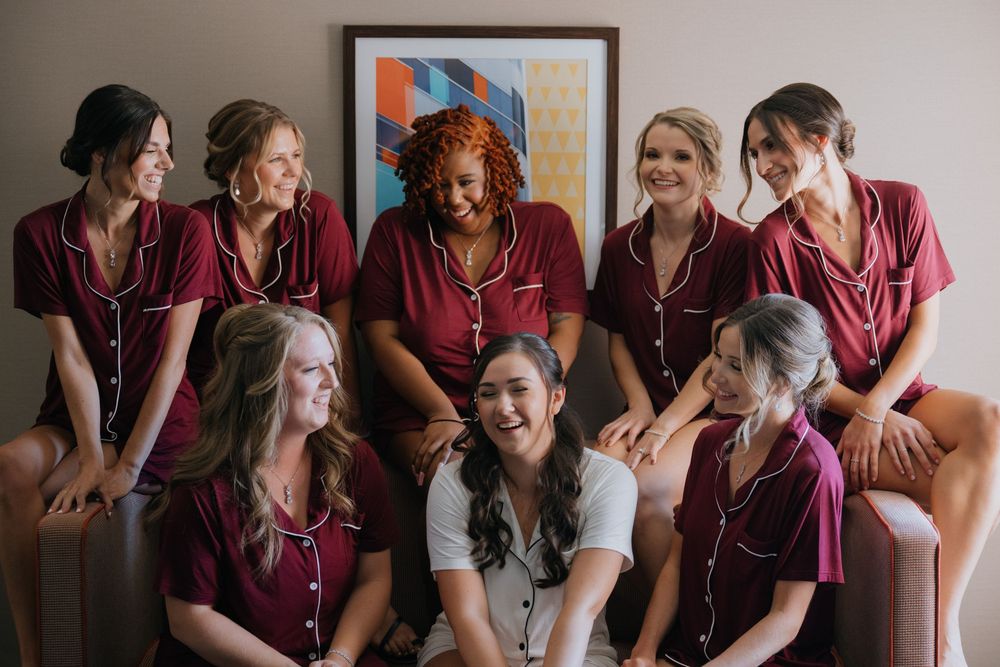 A group of bridesmaids in burgundy robes share joyful moments while getting ready for a wedding celebration.